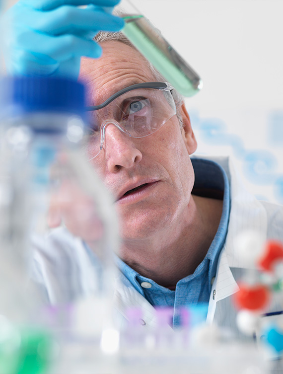 Ein Wissenschaftler betrachtet konzentriert etwas im Labor durch eine Schutzbrille.