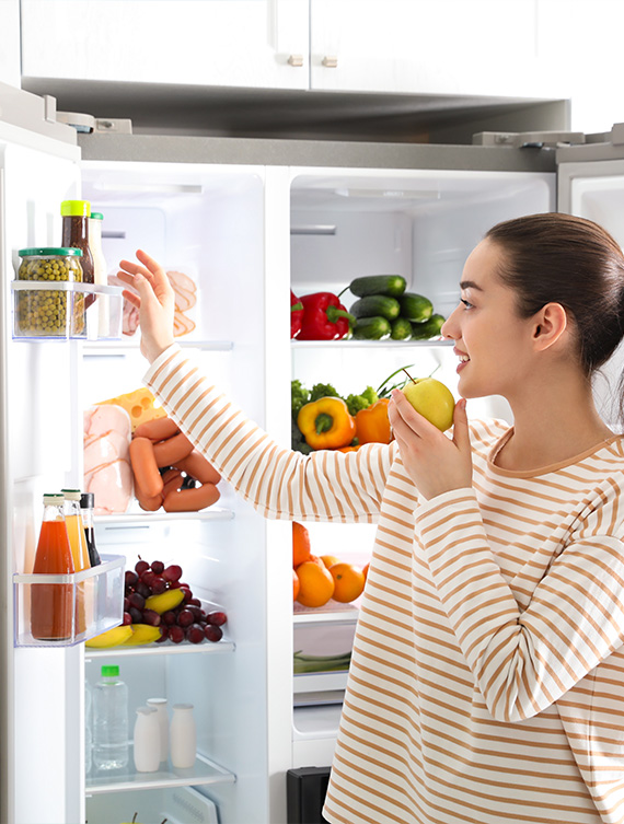 Eine Person nimmt Essen aus einem gut gefüllten Kühlschrank.